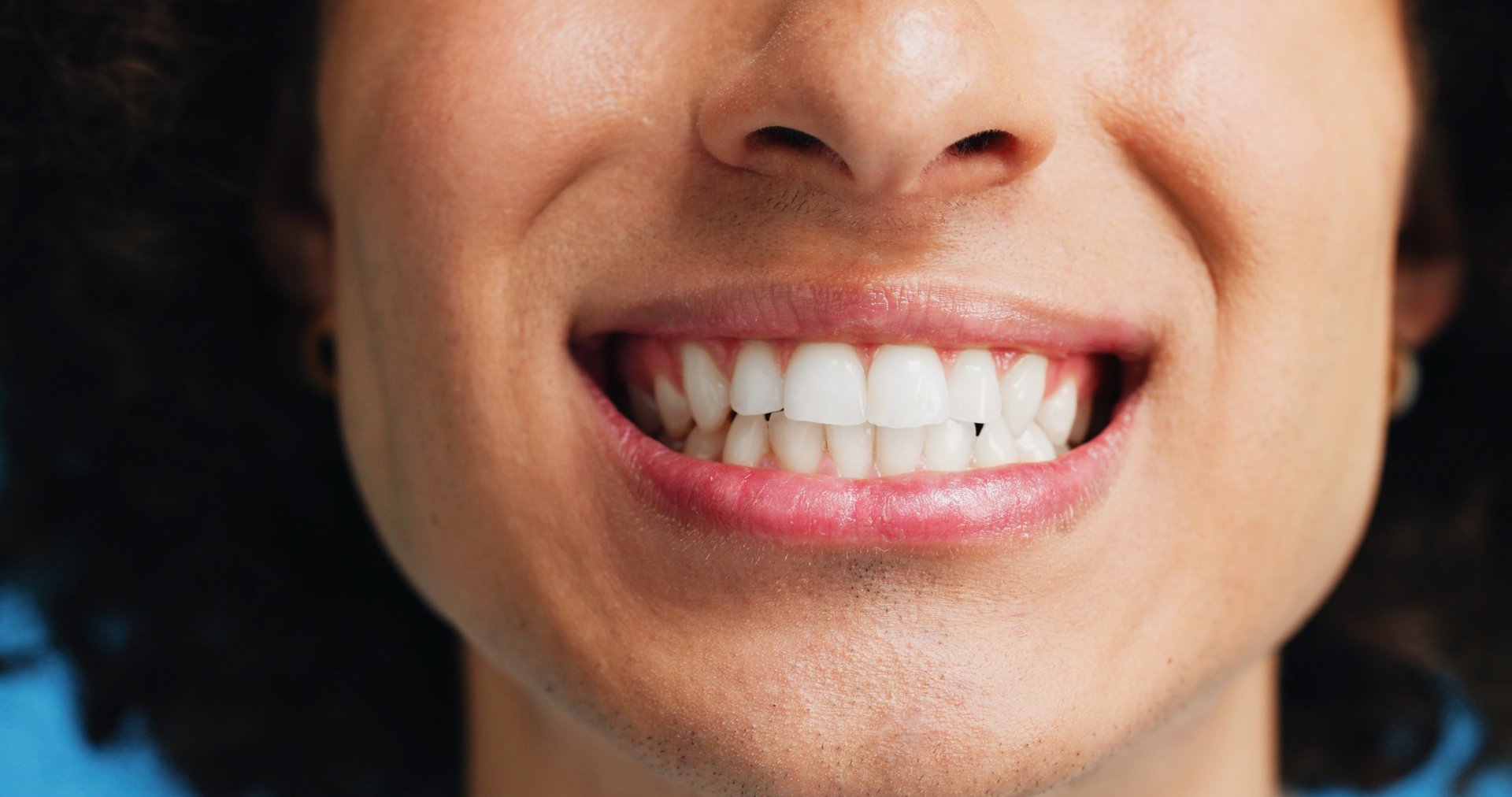 Person, teeth and mouth with smile for dental clean, hygiene or oral and gum care treatment. Closeup, lips and tooth whitening with dentist for cavity or plaque removal on a blue studio background.