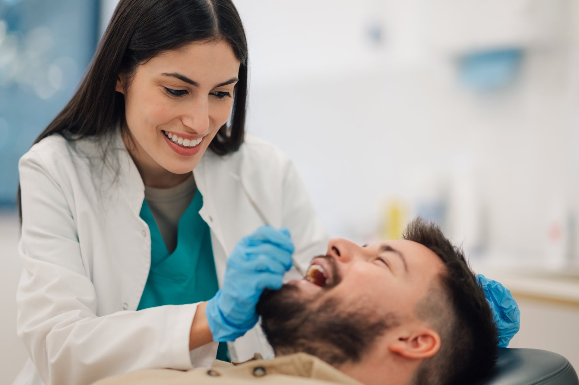 Female dentist is carefully examining the teeth of a male patient in her modern dental clinic