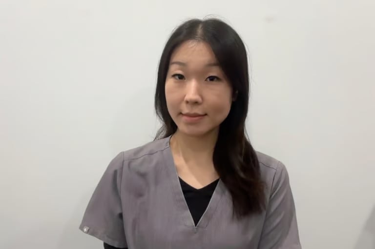 Portrait of a woman with long dark hair wearing a gray and black top against a white background