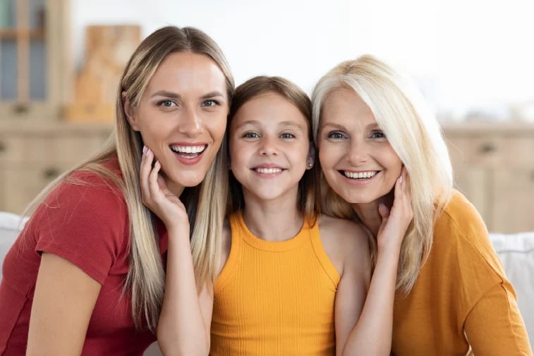Three smiling women posing together indoors, wearing red, yellow, and orange tops