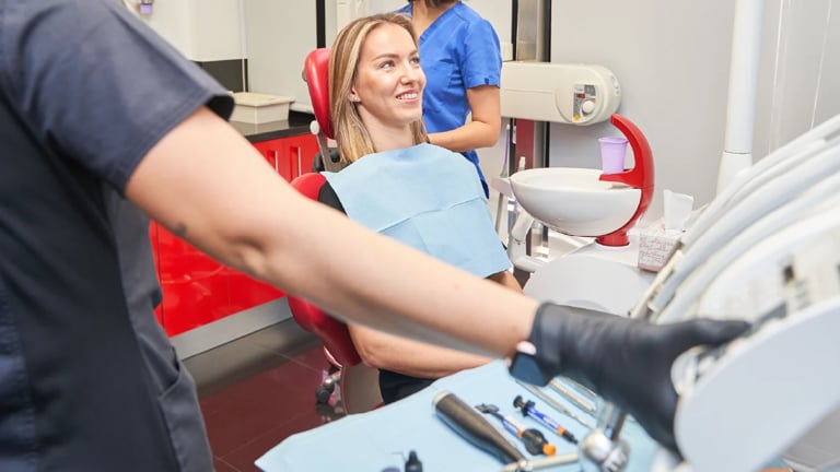 Patient in dental bib receiving examination from dentist wearing black gloves in modern dental clinic
