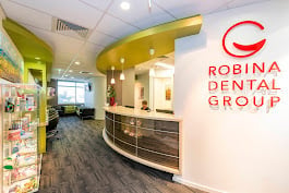 Modern dental office reception area with yellow ceiling accents, reception desk, and Robina Dental Group branding on wall