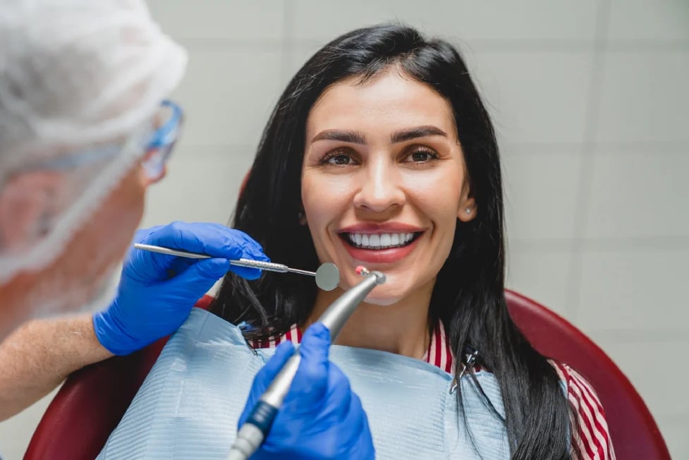 Smiling woman receiving dental examination from dentist wearing blue gloves during checkup