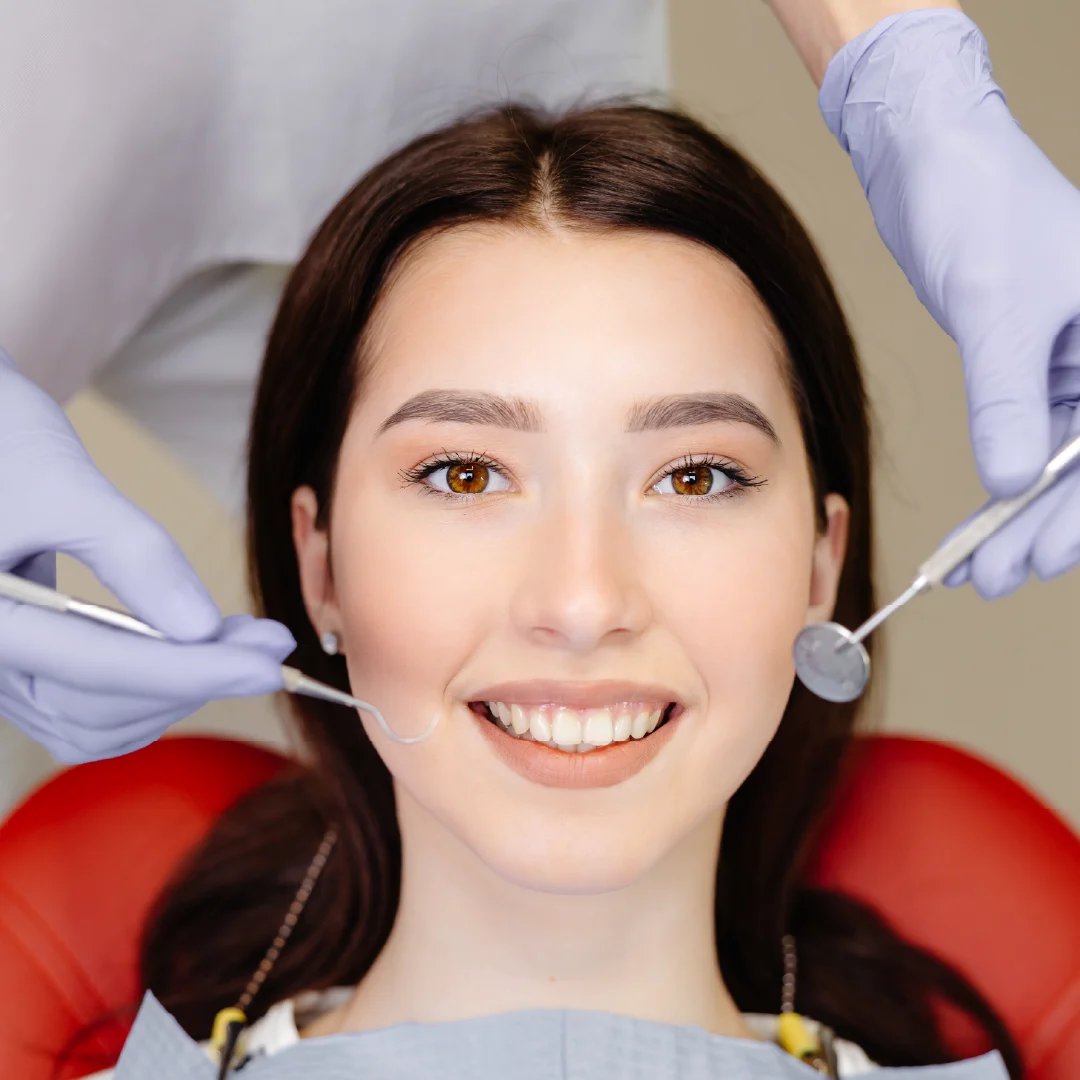 Woman smiling in dental chair with dentist holding mirror and tools during dental examination