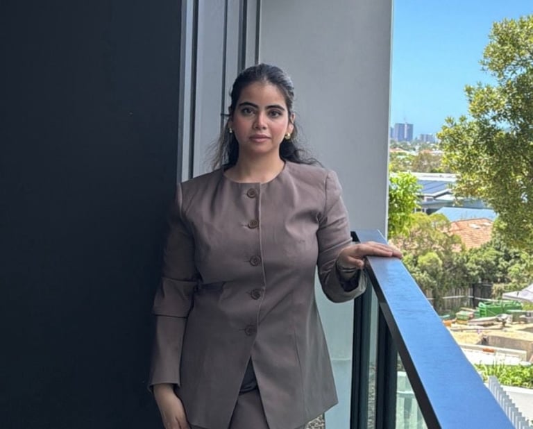 Woman in brown blazer leaning on a blue railing on a balcony with city views